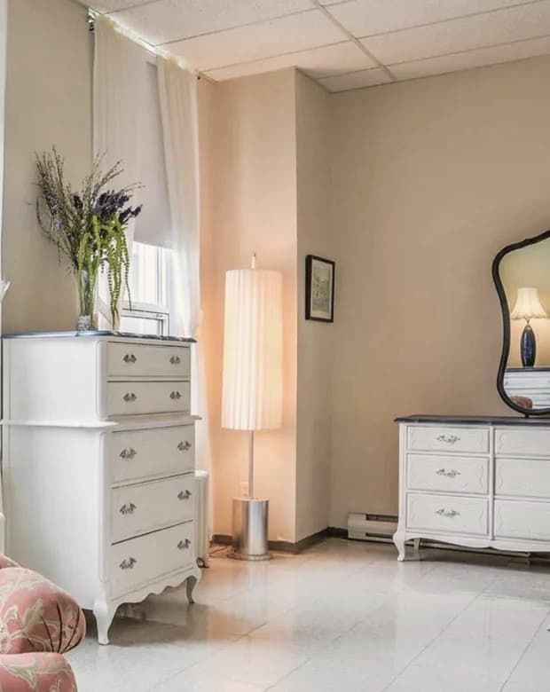 Une commode, un lampadaire et le rideau d’une fenêtre de chambre